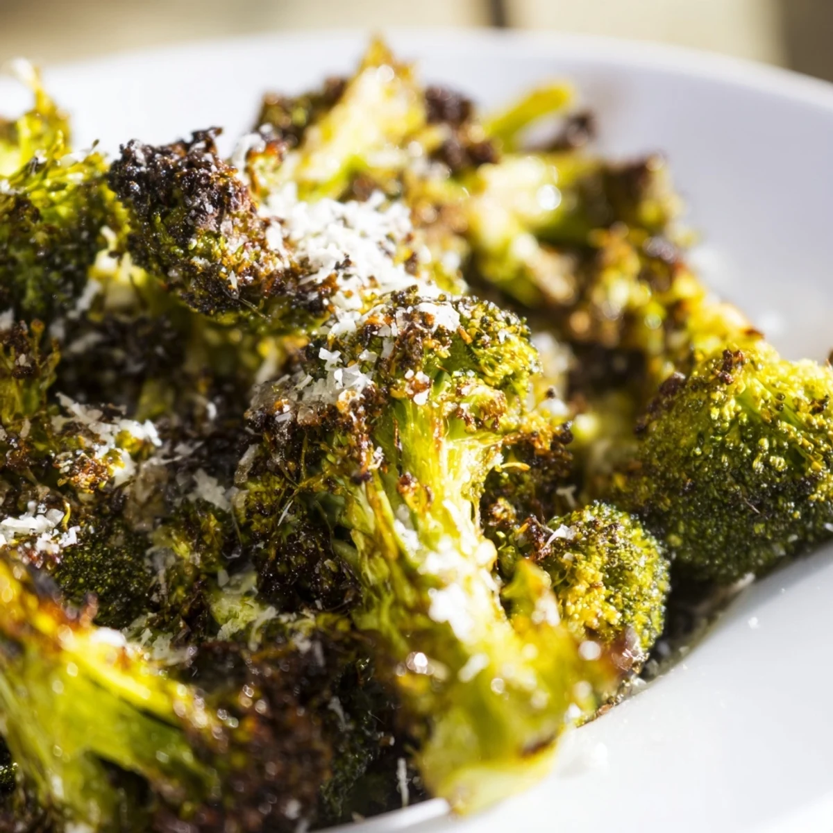 Freshly roasted broccoli florets with golden Parmesan and minced garlic on a rustic baking sheet.