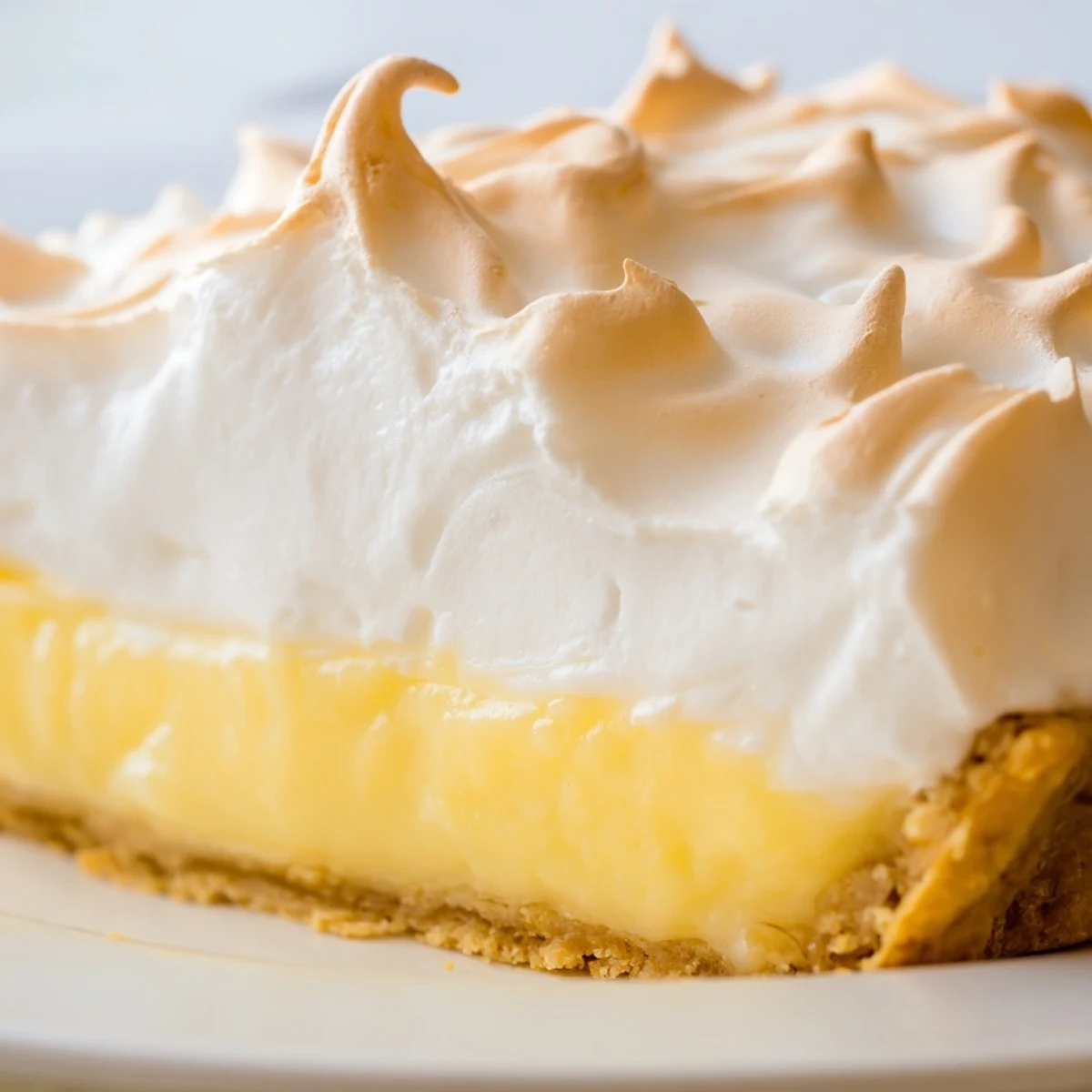 Overhead view of Lemon Meringue Pie with Graham Cracker Crust, with a silver pie server cutting a clean slice to reveal silky lemon filling and a crunchy crust.