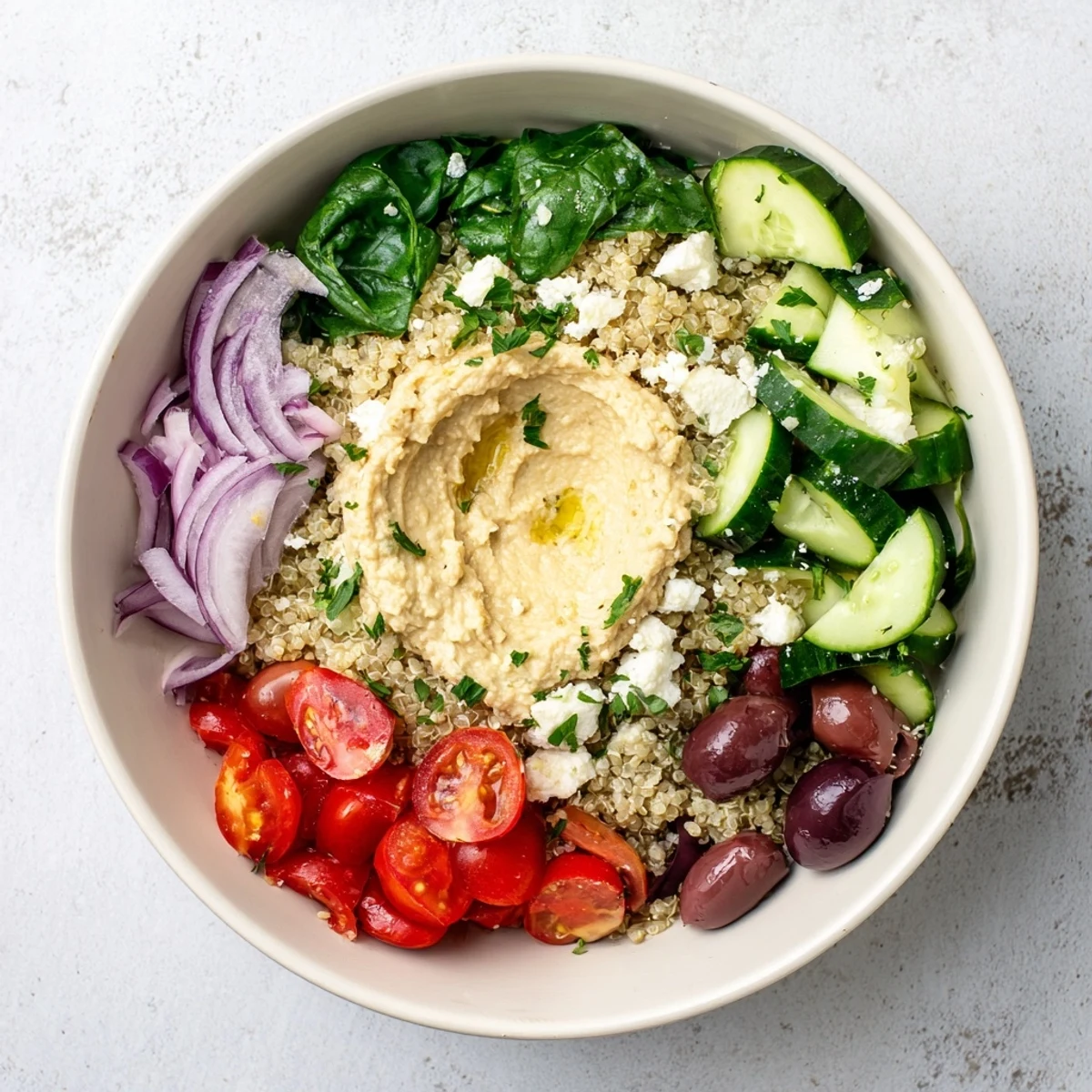 A vibrant Mediterranean Quinoa Bowl with hummus, Kalamata olives, and colorful veggies on a white plate.