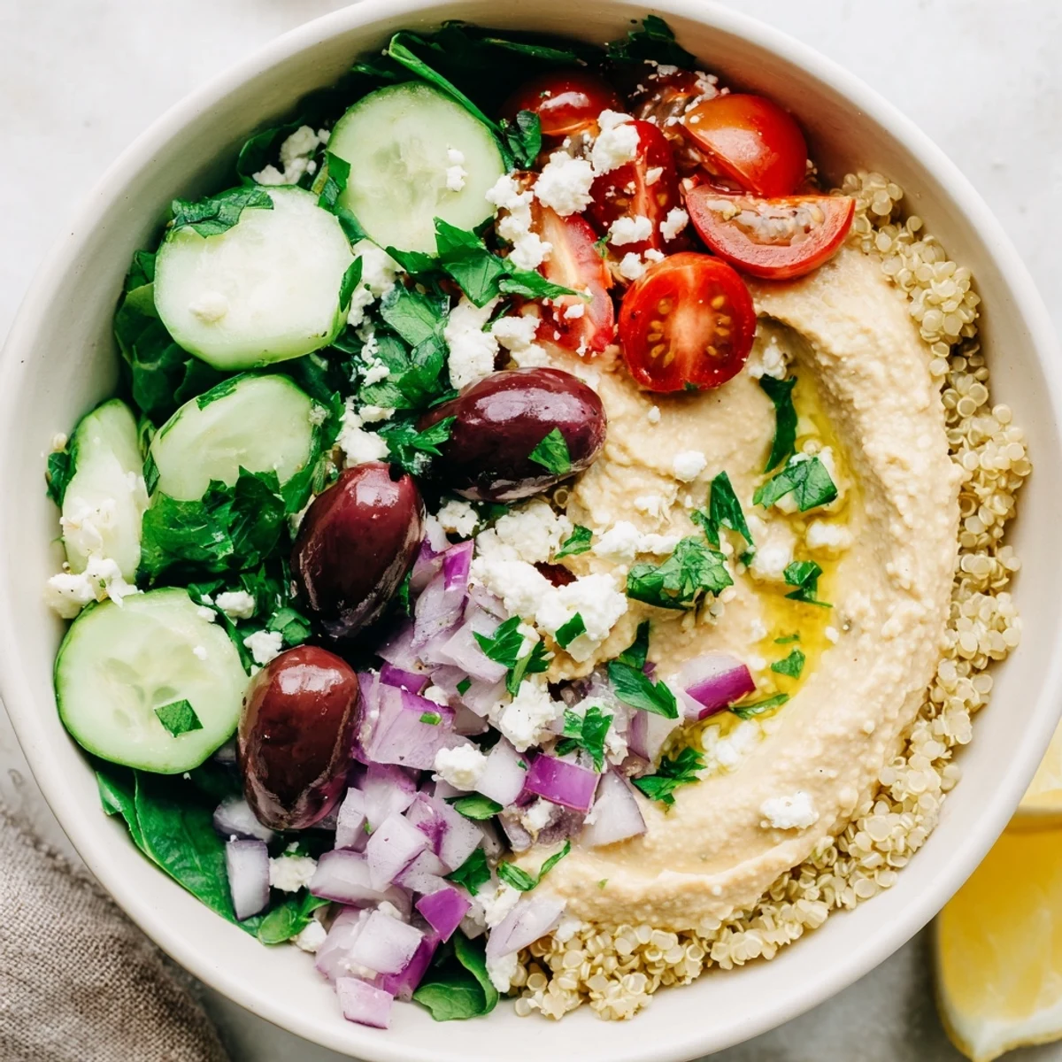 A fresh Mediterranean Quinoa Bowl topped with creamy hummus, briny olives, feta, and a lemon-herb drizzle.