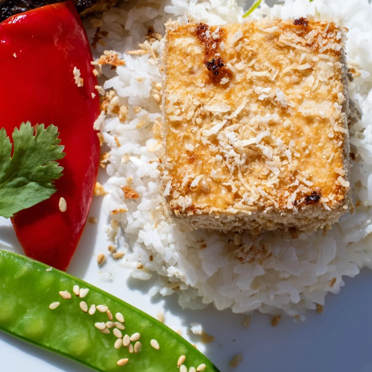 Crispy Coconut Tofu over jasmine rice with colorful stir-fry vegetables, garnished with sesame seeds and lime wedges.
