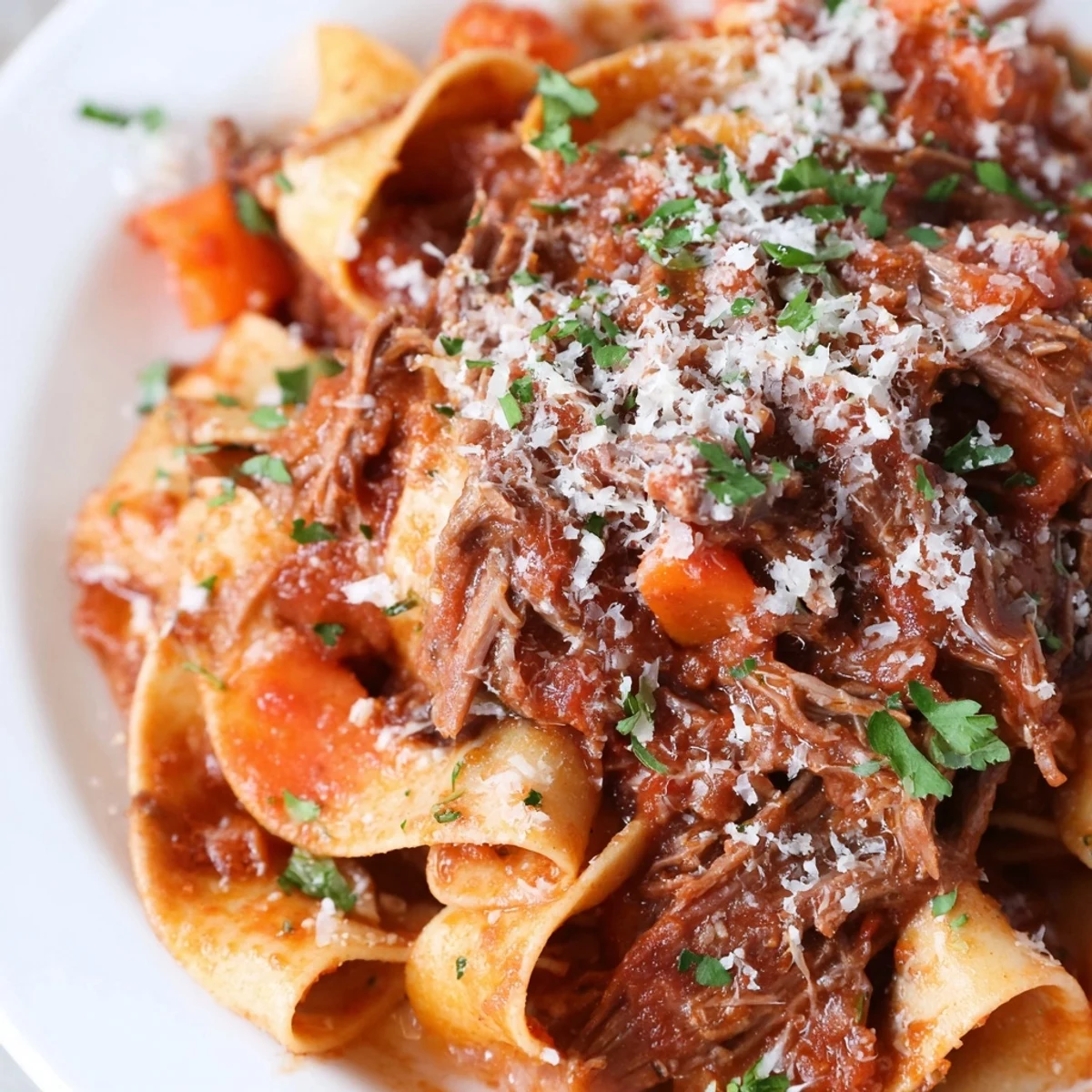 A hearty plate of Slow Cooker Beef Ragu with Pappardelle Pasta, featuring wide noodles coated in a rich, deep red tomato sauce, ready to serve.