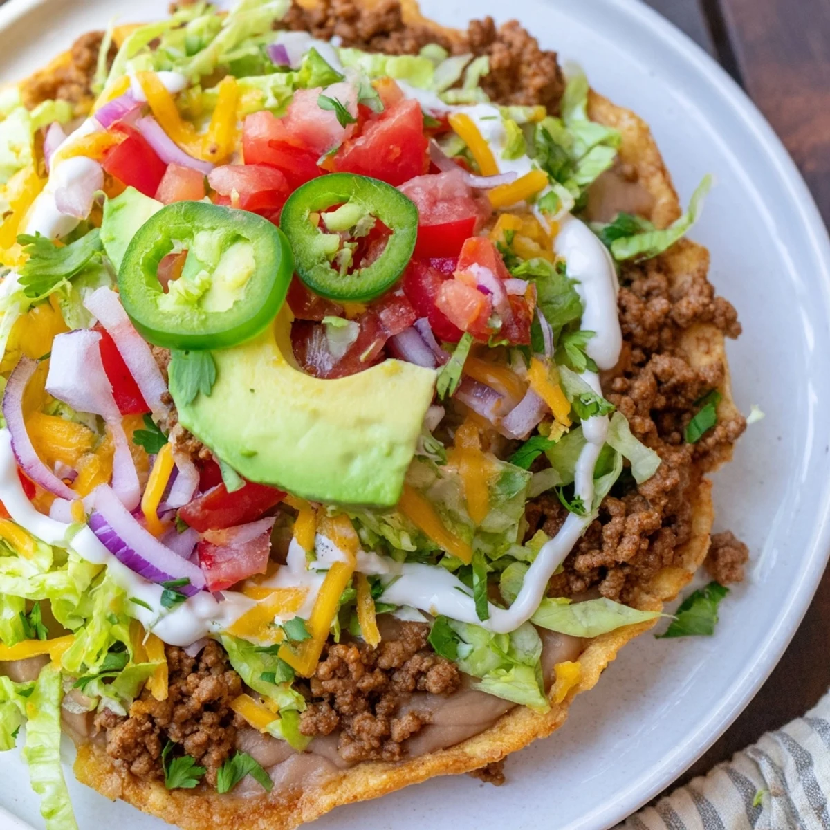 Golden tostada shells piled high with savory ground beef, refried beans, diced avocado, and colorful toppings for a festive meal.  