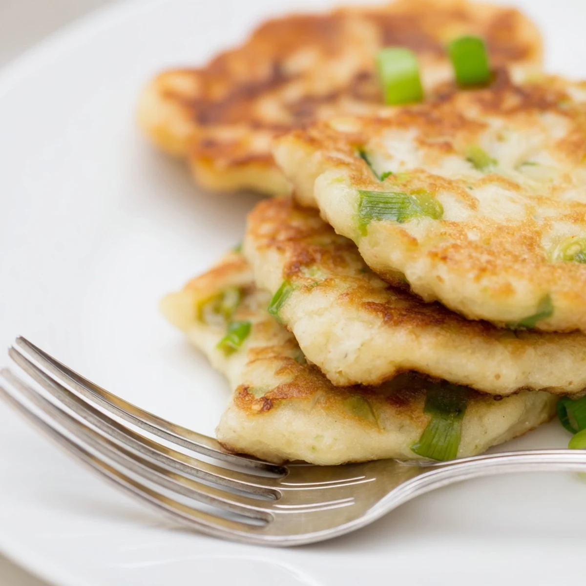 A close-up of crispy Irish Potato Cakes with Scallions, showcasing tender potato insides and vibrant green onion flecks.