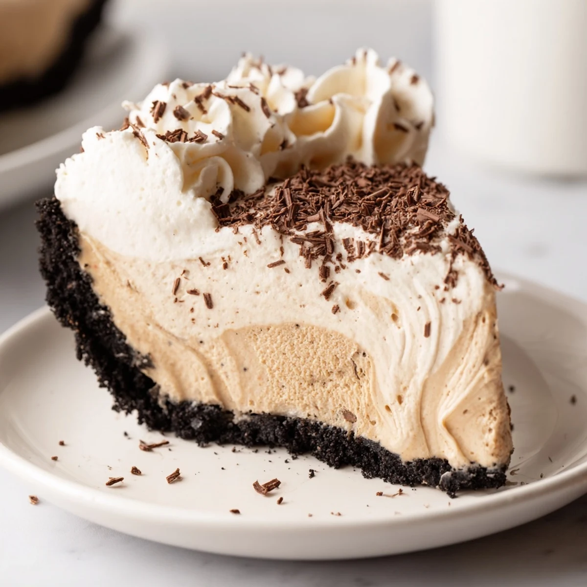 A slice of rich Irish Cream Cheesecake on a white plate with whipped cream and chocolate shavings, ready to serve.