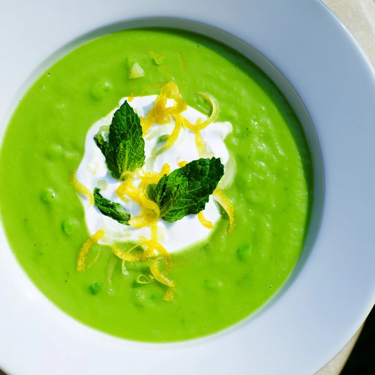 A bowl of Spring Pea Soup with Mint and Crème Fraîche, garnished with fresh mint leaves and a creamy swirl.