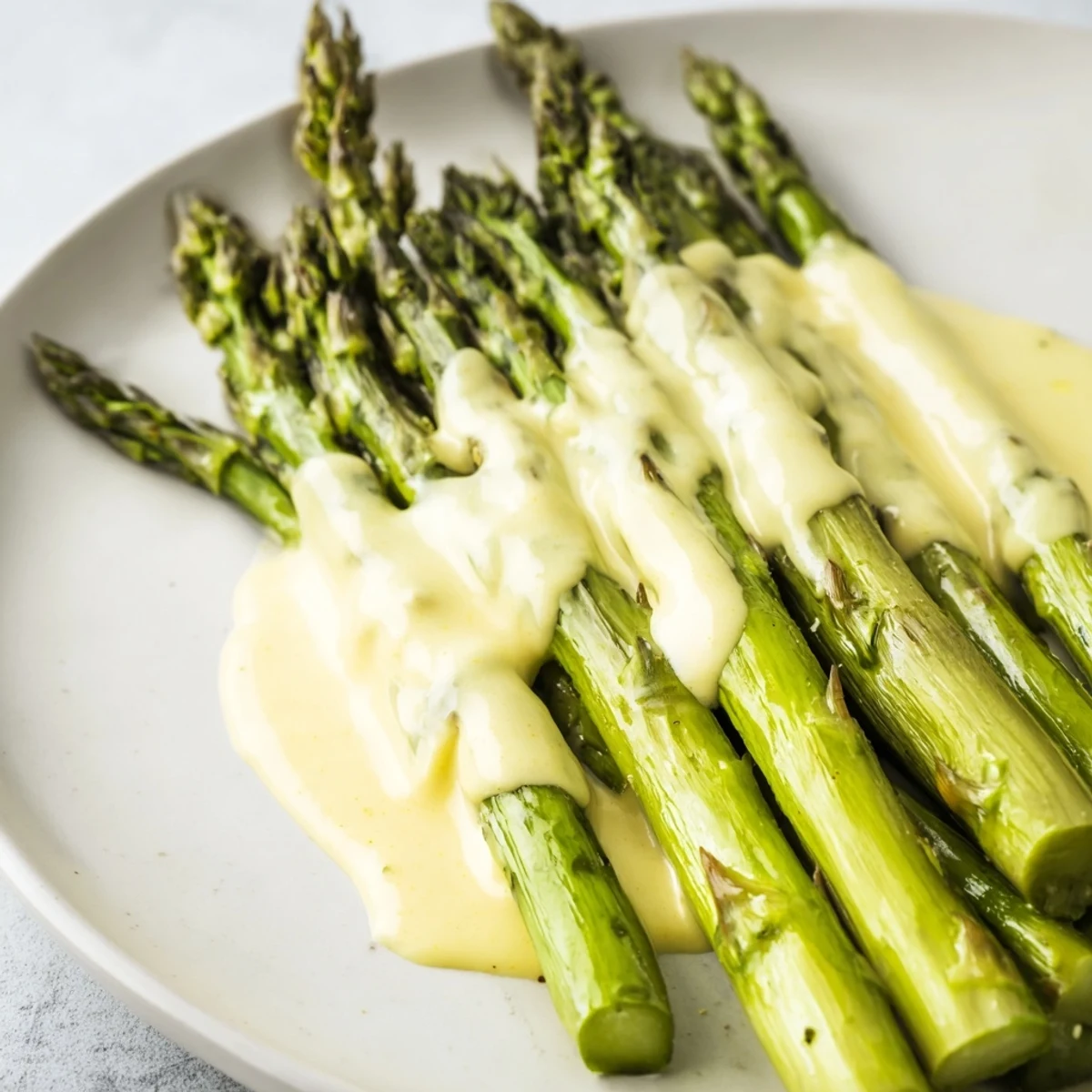 Golden roasted asparagus with hollandaise sauce glistening on a white plate, garnished with fresh chives.