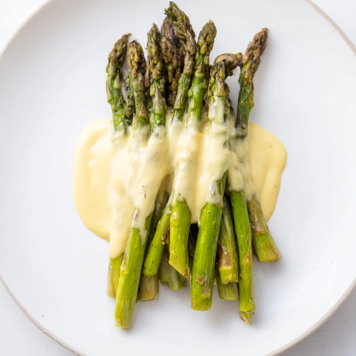 Roasted asparagus with hollandaise sauce arranged neatly, the creamy sauce drizzled over tender green spears.