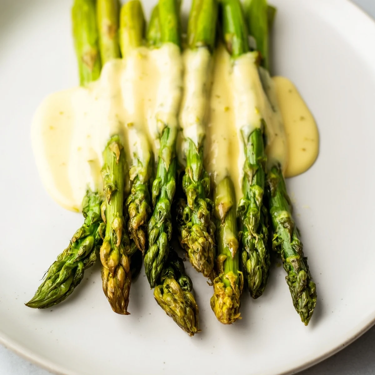 Freshly roasted asparagus with hollandaise sauce served warm, the bright green spears topped with velvety sauce.