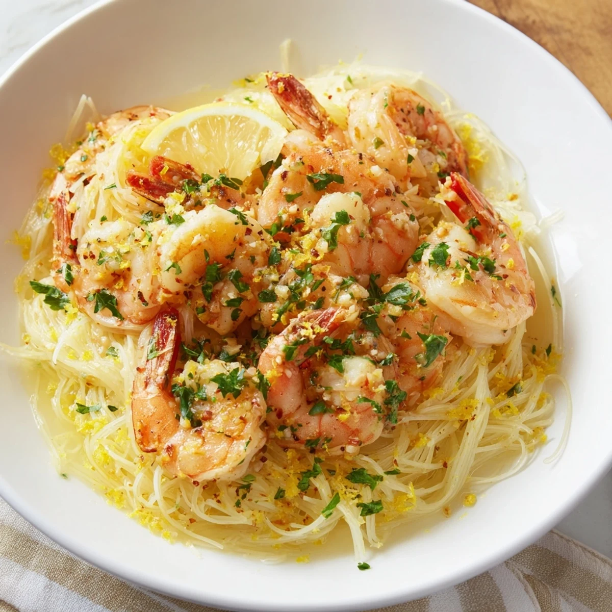 A close-up view of Lemon Garlic Butter Shrimp with Angel Hair, served hot in a white bowl with a lemon wedge.
