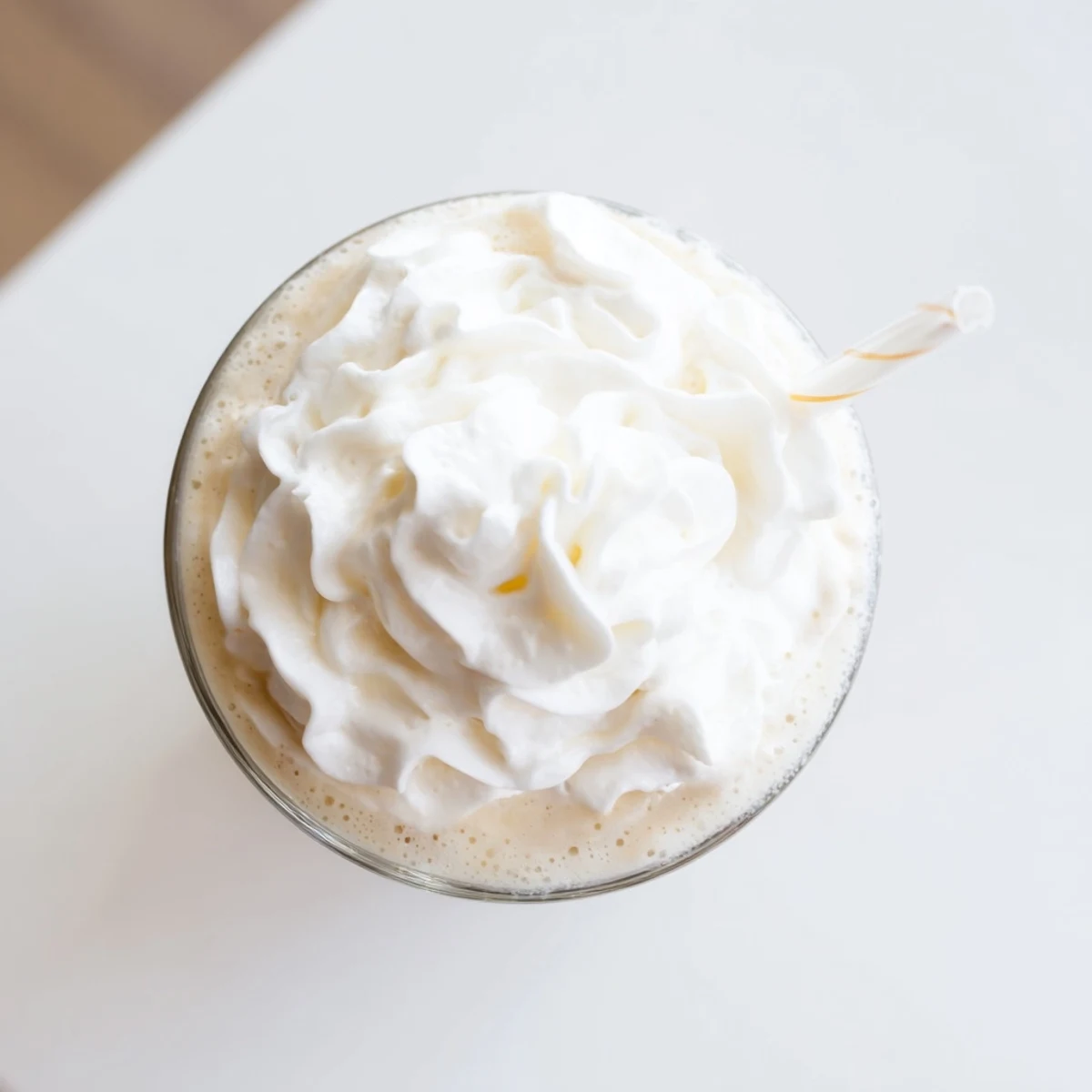 Two tall glasses filled with Starbucks Vanilla Bean Frappuccino and a sprinkle of ice cubes beside a blender on a sunny kitchen counter.