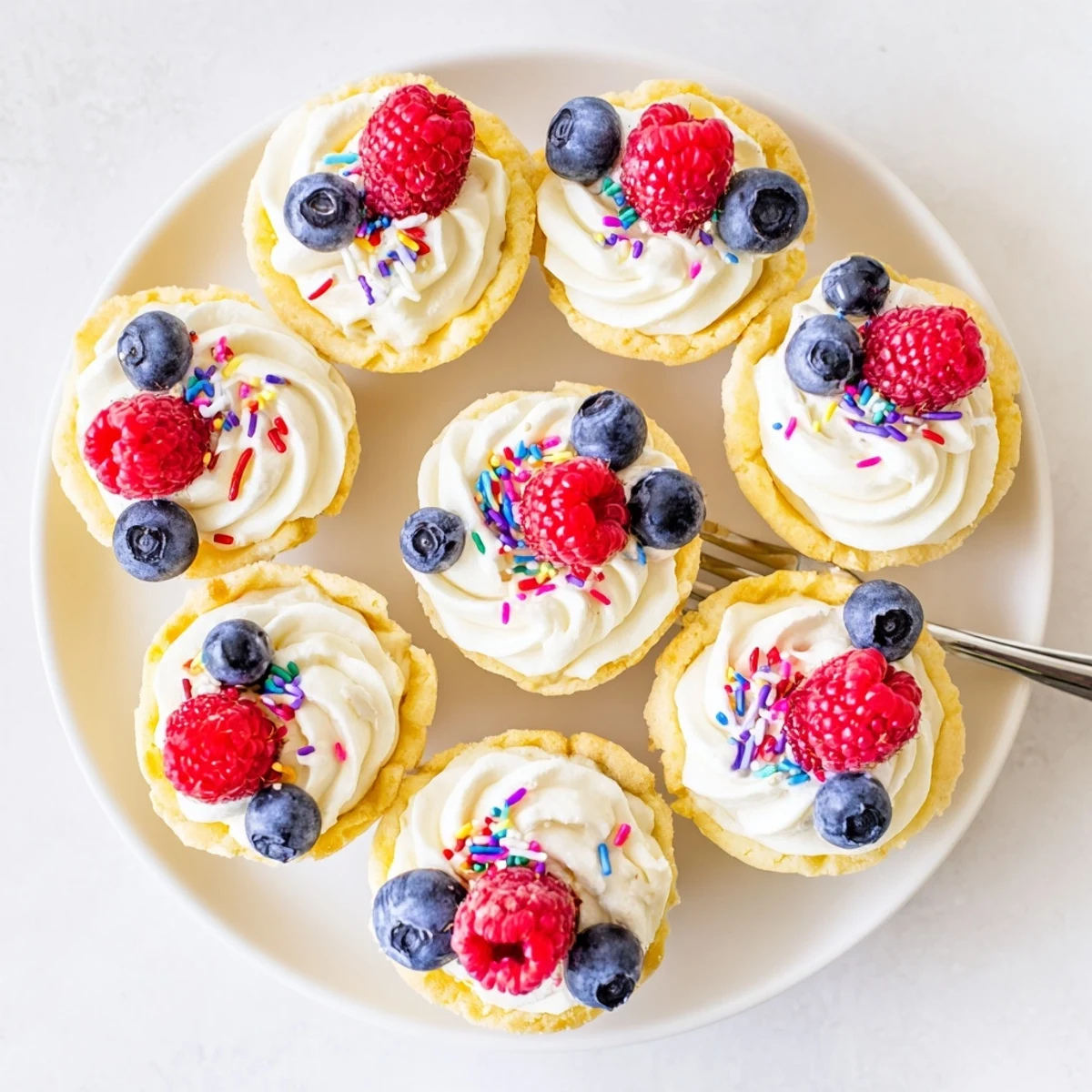Golden-baked Sugar Cookie Cups in a mini muffin tin, filled with fluffy vanilla cream and topped with fresh raspberries for a party-ready dessert.