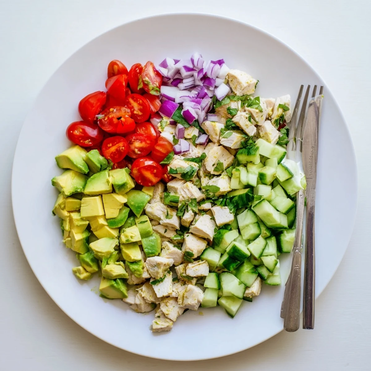 A close-up of a vibrant bowl of Avocado Chicken Salad, featuring tender chicken, bright green avocado chunks, red tomatoes, and fresh cilantro on mixed greens.