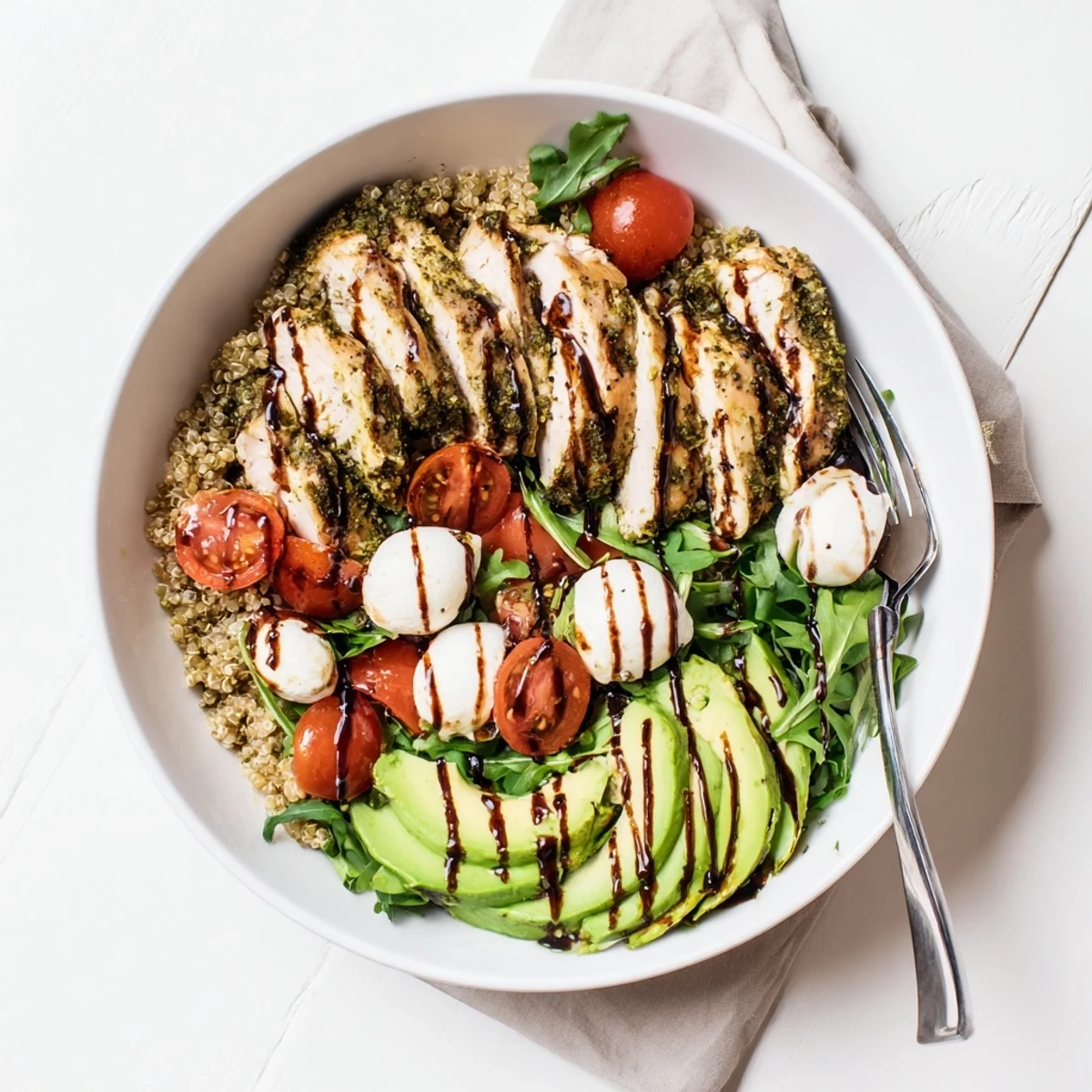 Juicy pesto-marinated chicken slices rest on fluffy quinoa with fresh mozzarella and tomatoes in this Pesto Chicken Caprese Grain Bowl.