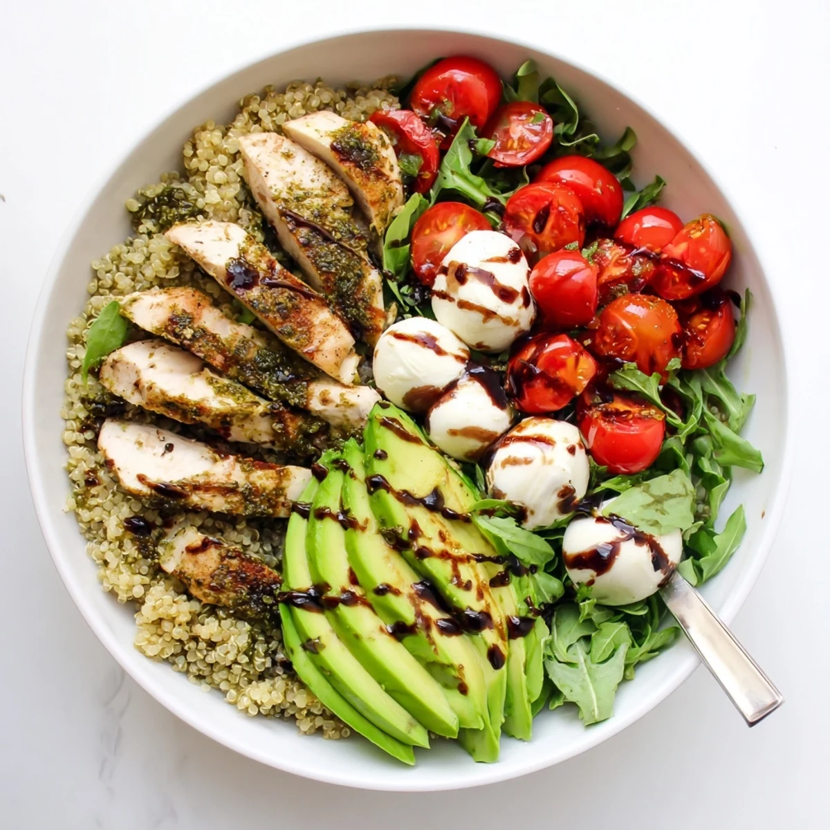 Vibrant red tomatoes, creamy mozzarella balls, and green basil leaves top the Pesto Chicken Caprese Grain Bowl beside sliced avocado.