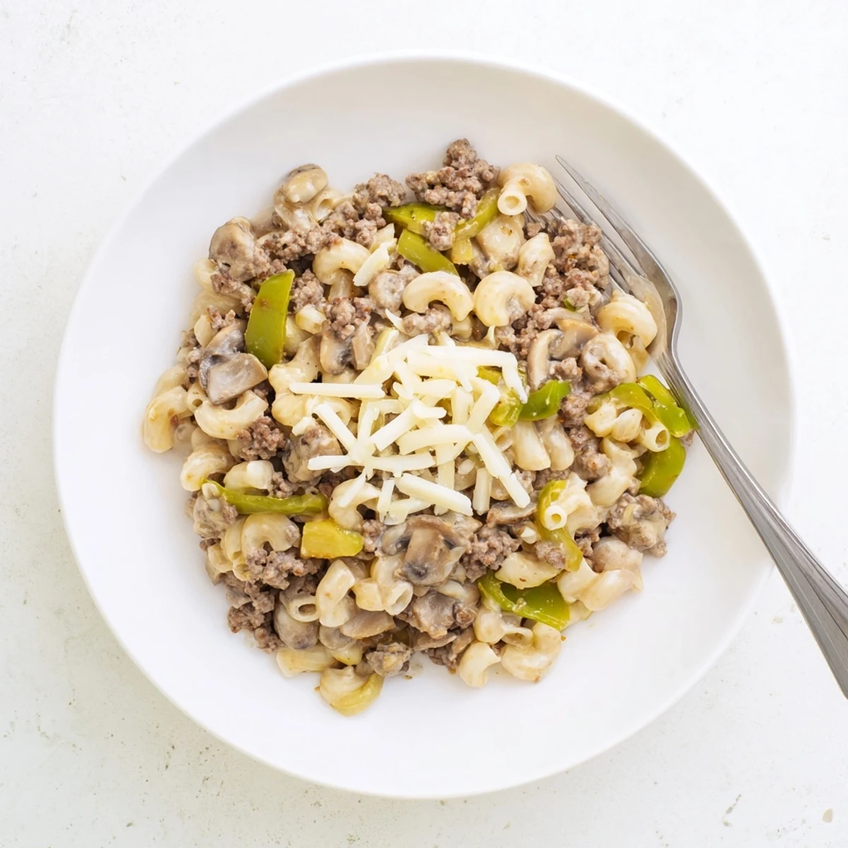 Close-up of Easy High Protein Philly Cheesesteak Mac revealing juicy ground beef, mushrooms, and bell peppers mingling in a rich, creamy sauce inside a white bowl.