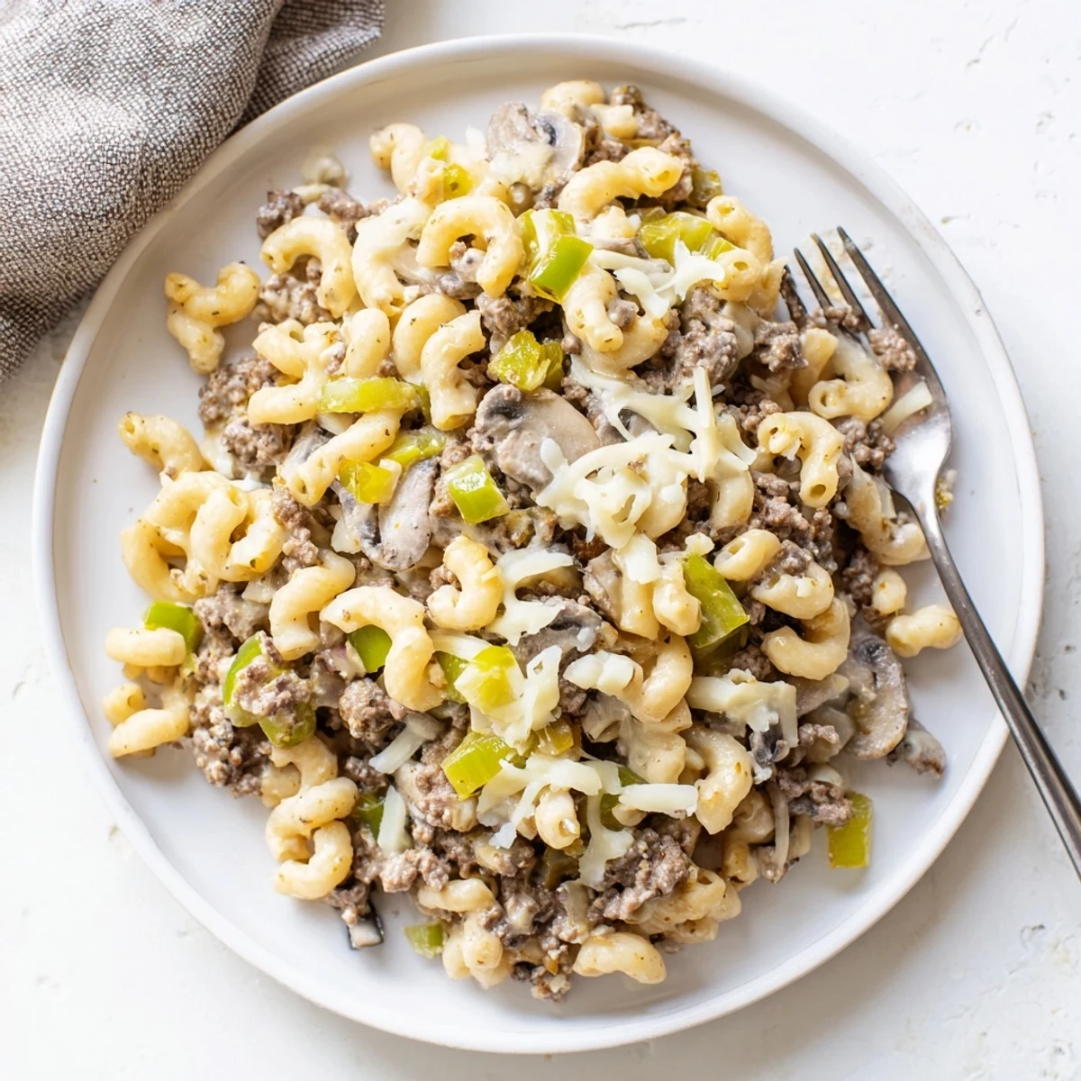 Plated Easy High Protein Philly Cheesesteak Mac with a golden cheesy top, garnished with fresh parsley alongside a crisp green salad for a balanced dinner.