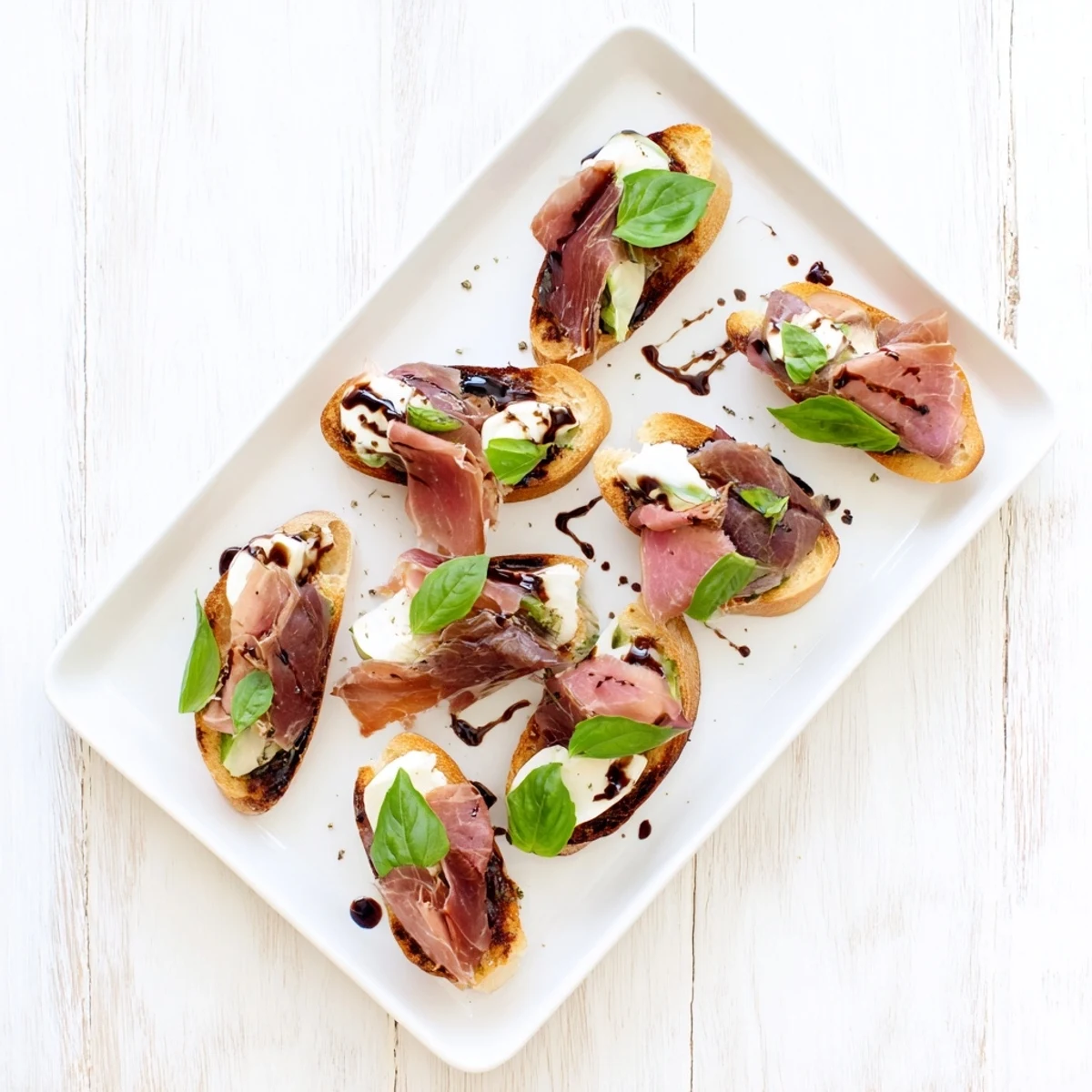 Crispy toasted baguette slices topped with melted mozzarella, roast beef, and prosciutto with fresh basil and balsamic drizzle for a delicious Mozzarella Beef Prosciutto Crostini appetizer.