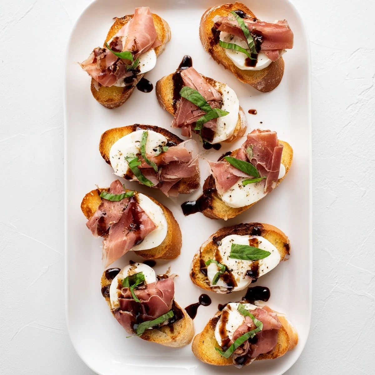 Warm Italian-inspired Mozzarella Beef Prosciutto Crostini arranged on a platter, garnished with fresh basil leaves and a light balsamic reduction, ideal for a party snack.