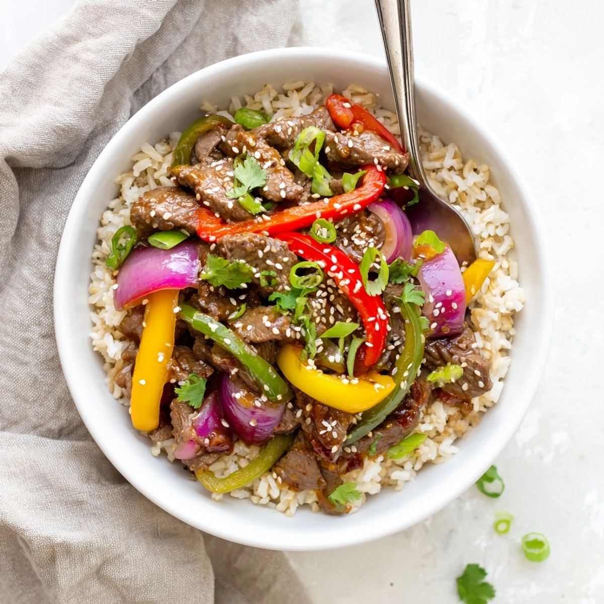 Healthy Beef and Pepper Rice Bowl in a white bowl garnished with sesame seeds and fresh cilantro leaves.