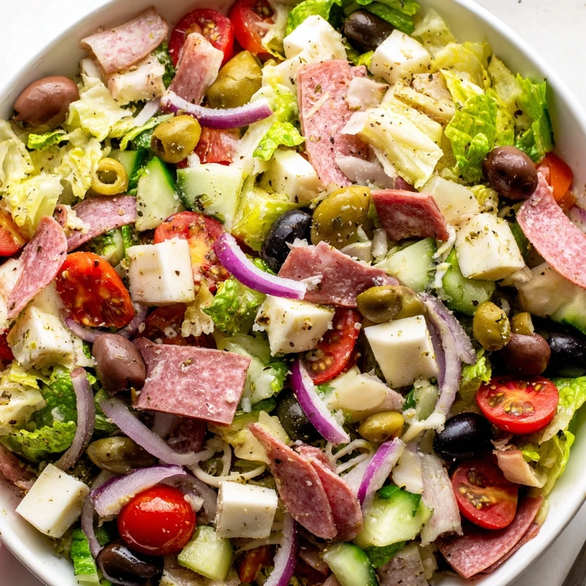 Vibrant Italian chopped salad bowl with fresh romaine, salami, and tangy homemade dressing drizzled over colorful vegetables