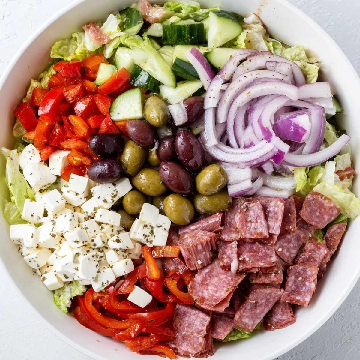 Colorful Italian chopped salad featuring mozzarella, olives, and zesty dressing in a white serving bowl