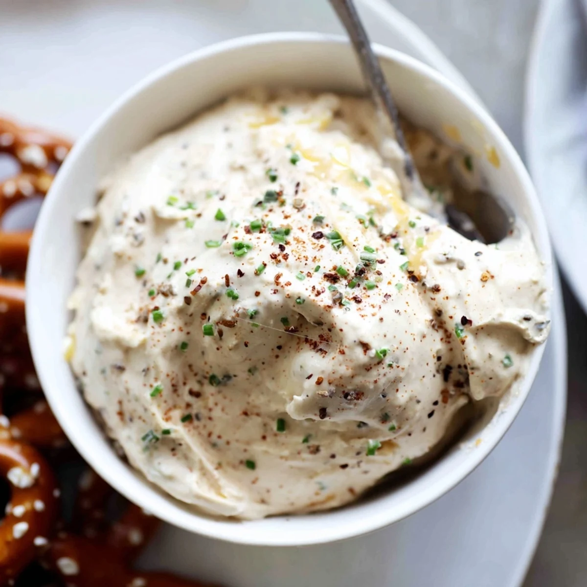 Rich cheesy savory pretzel dip in a white bowl, garnished with green onions
