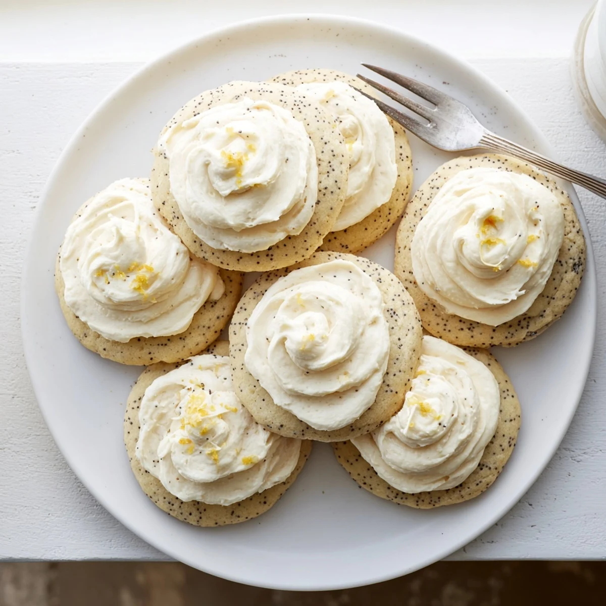 Close up of bright lemon cookies speckled with poppy seeds topped with tangy cream cheese frosting