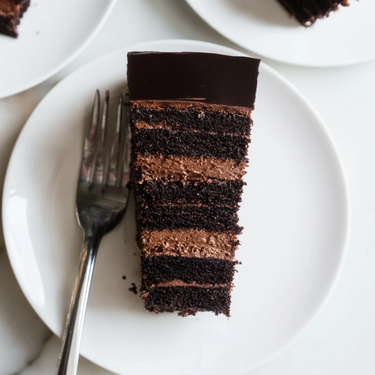 Rich dark chocolate mousse cake with glossy glaze draping over velvety layered slices on a white dessert plate