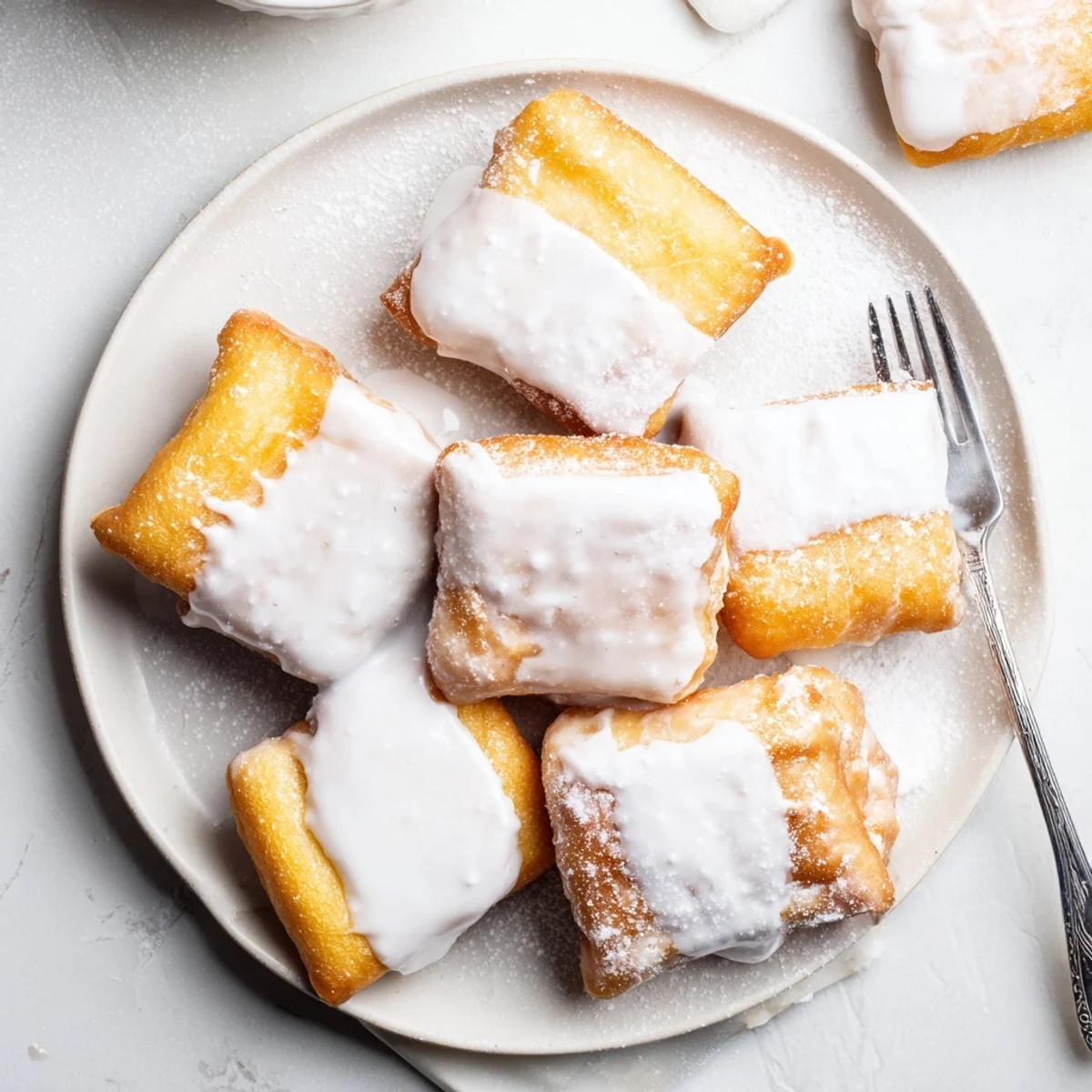Fluffy fried beignet squares drizzled with sweet vanilla glaze and stacked for serving