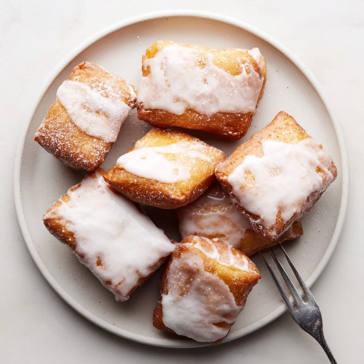 Warm buttermilk beignet squares coated in white icing and arranged on a white plate