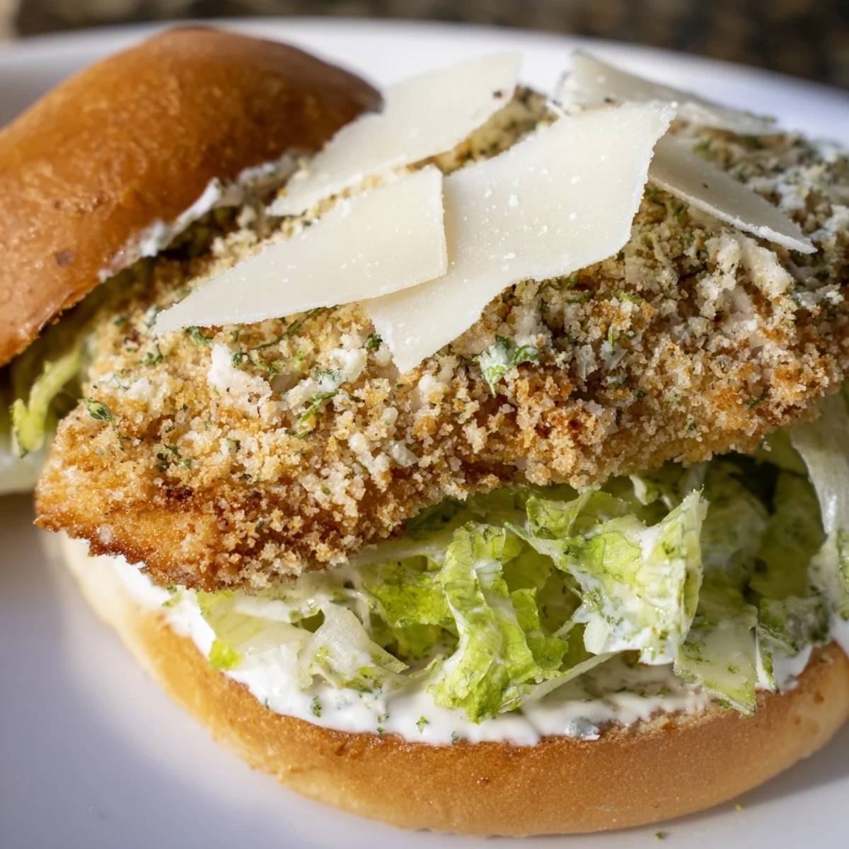 Handheld sandwich featuring breaded fried chicken drizzled with creamy Caesar sauce and crunchy lettuce layers