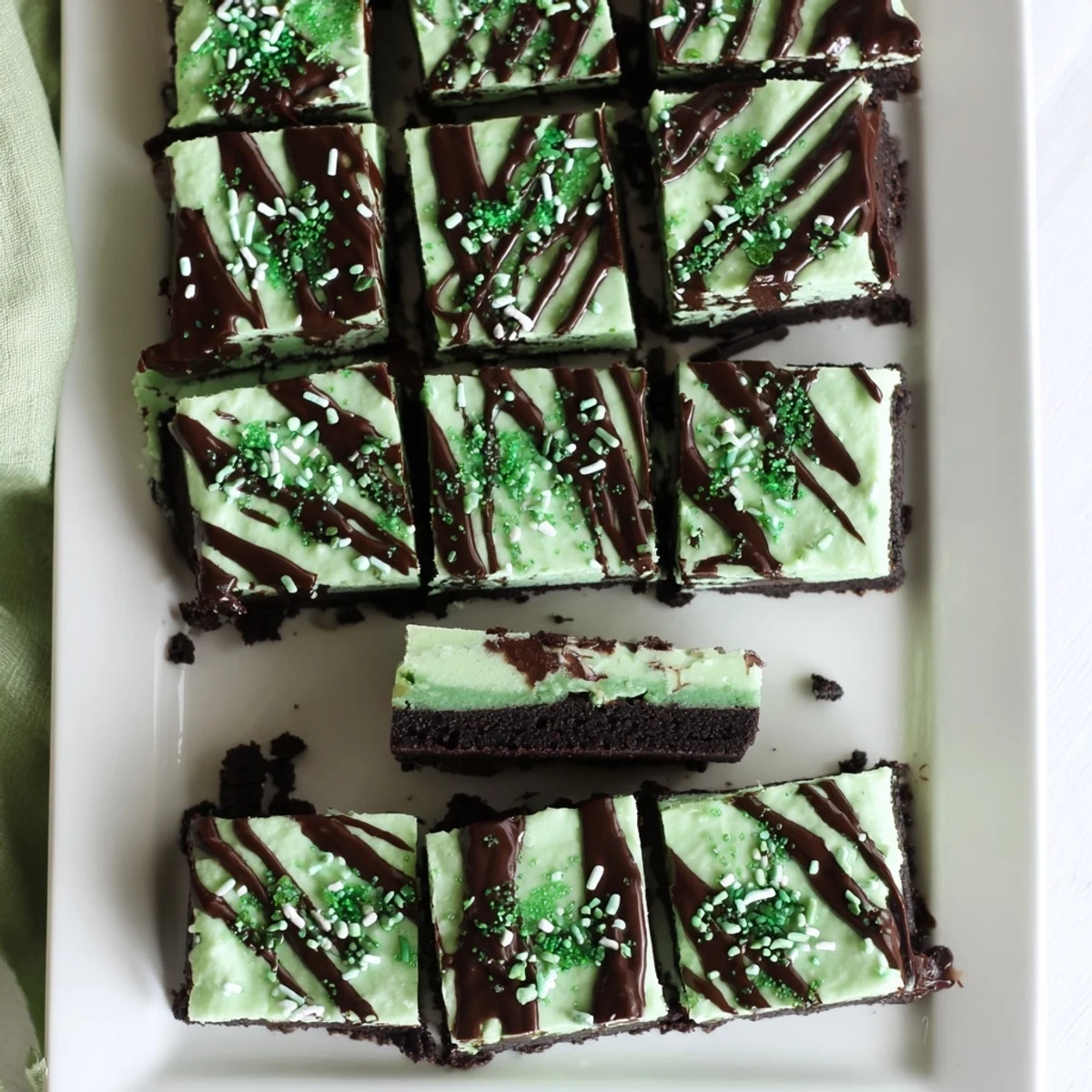 Decadent St. Patricks Irish mint cheesecake fudge squares on chocolate cookie crust with dark chocolate drizzle and festive green sprinkles