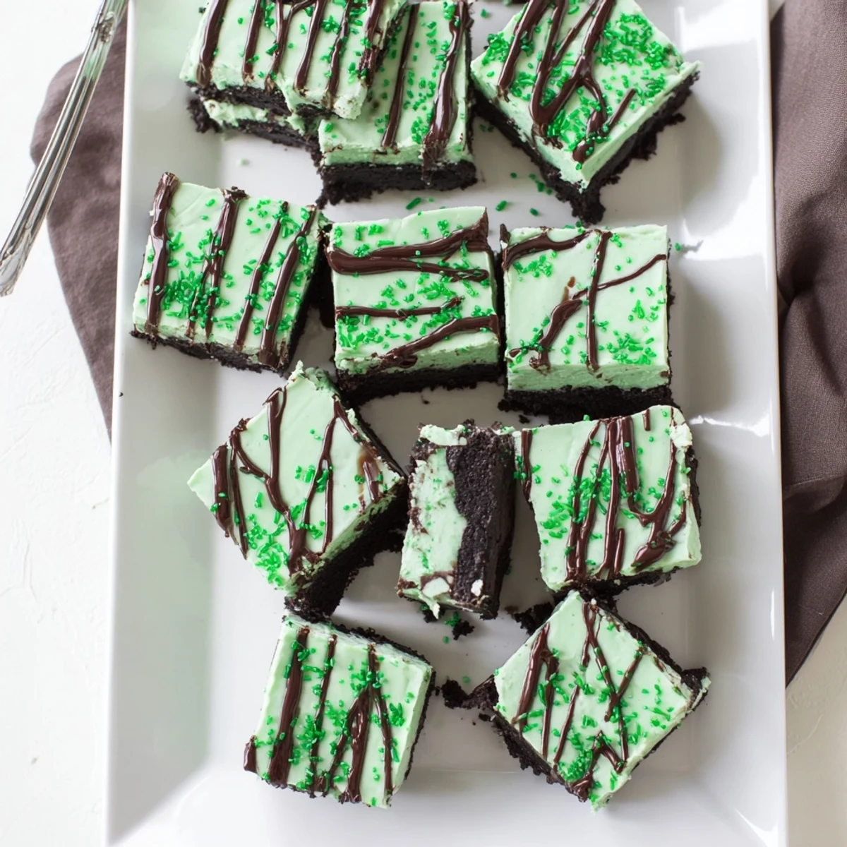 Green-tinted St. Patricks Irish mint cheesecake fudge squares featuring smooth mint cream cheese filling and dark chocolate ganache topping