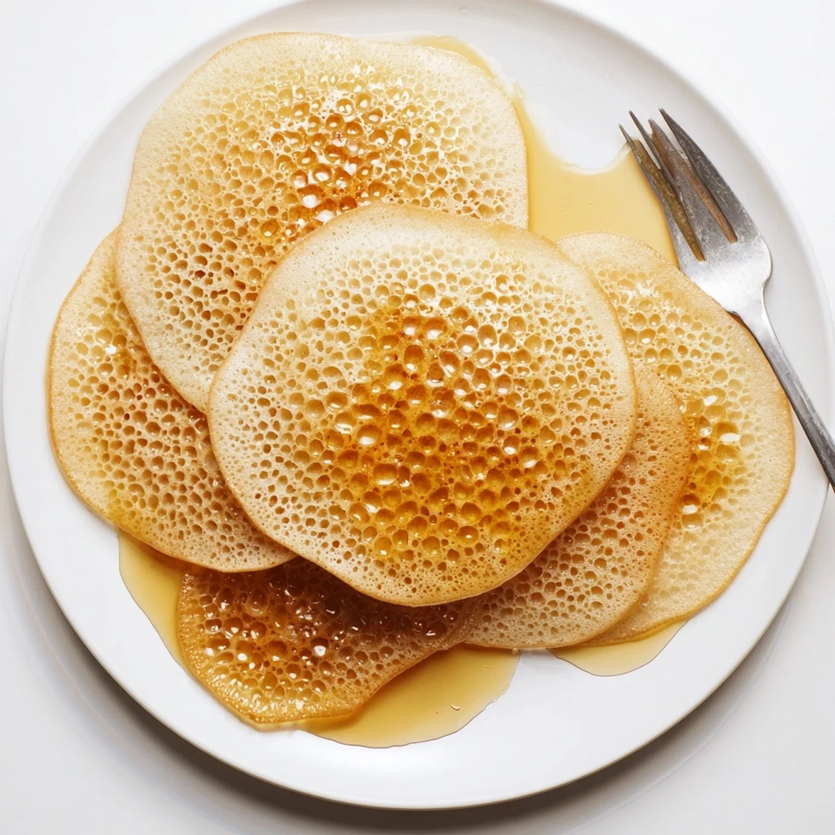 Golden baghrir Moroccan pancakes topped with melted butter and honey, showcasing signature honeycomb bubbles