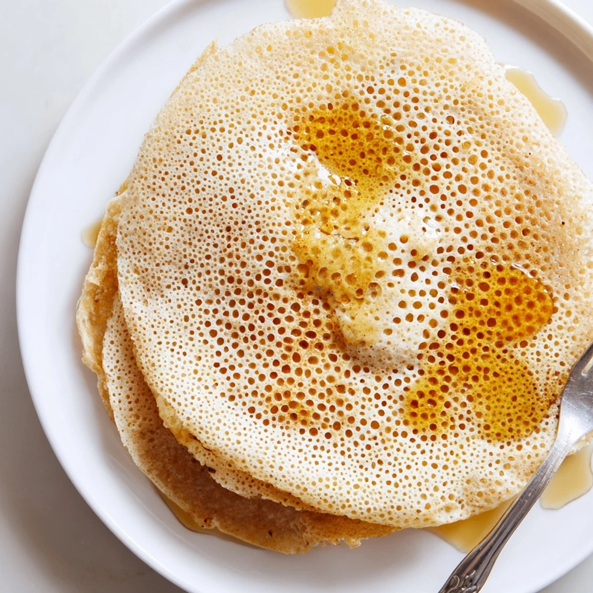 Light spongy baghrir stacked on serving plate, drizzled with sweet honey for authentic Moroccan breakfast