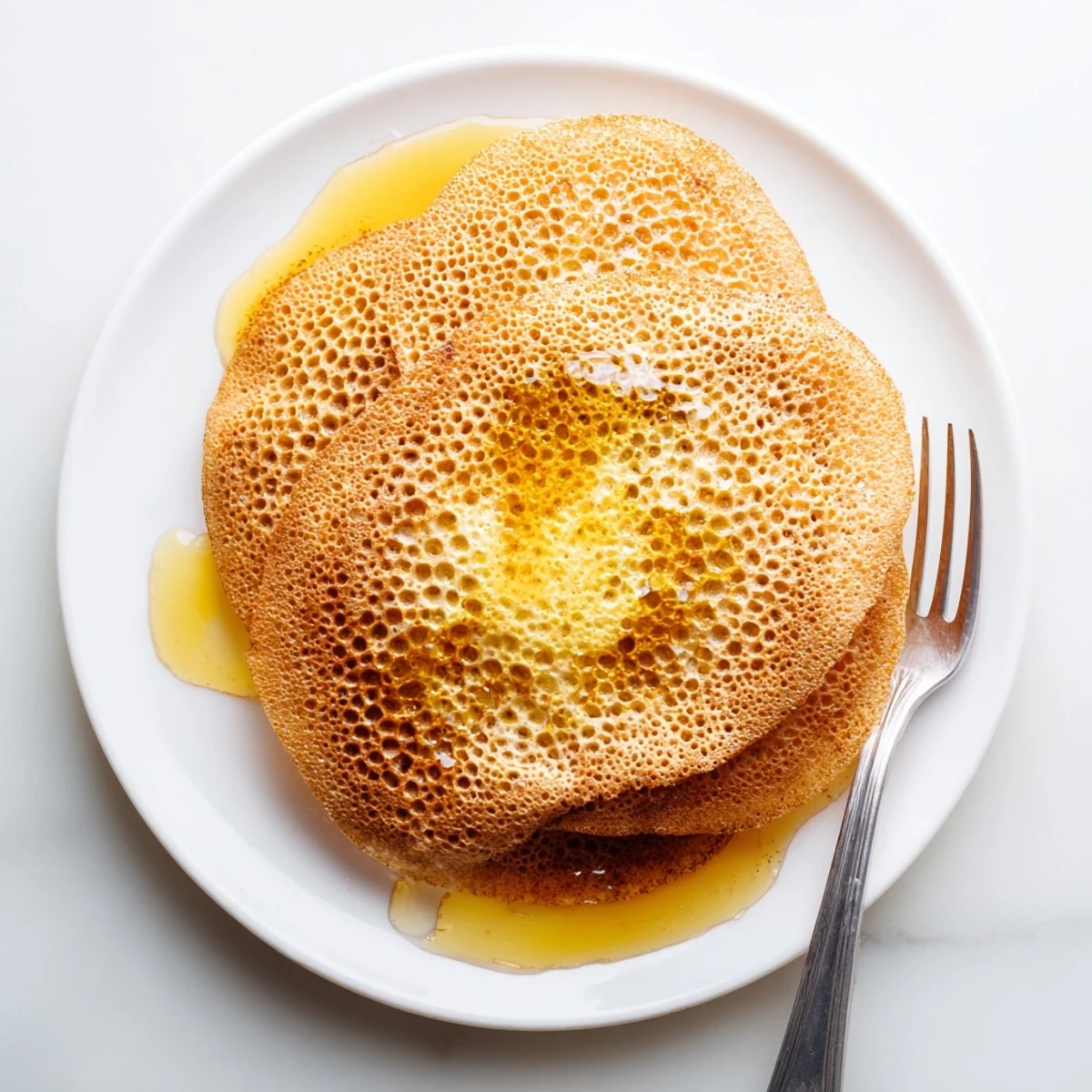 Freshly cooked baghrir displaying porous texture, served warm with butter and honey for traditional snack