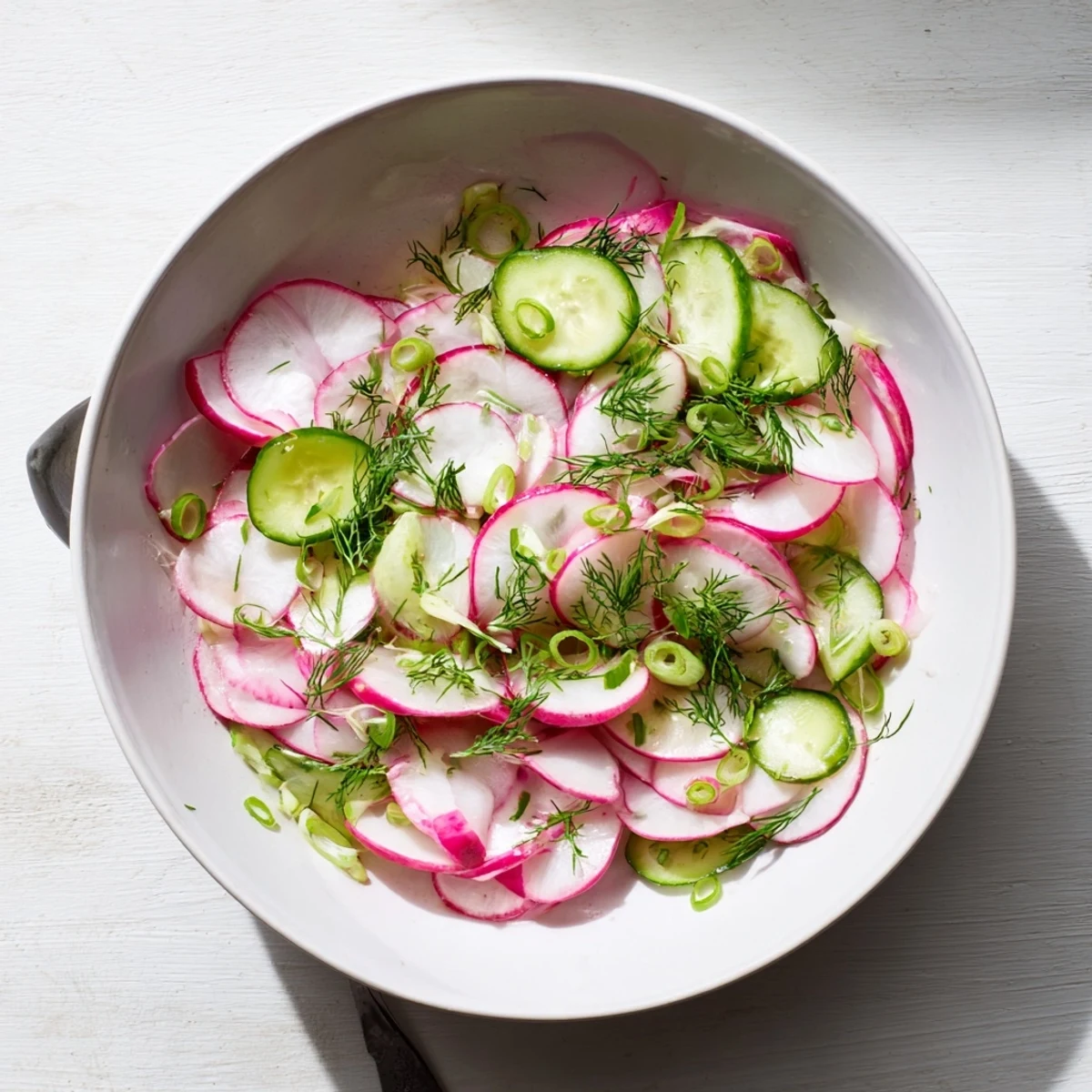 Fresh radish and cucumber salad arranged in a white serving bowl with vibrant green dill garnish