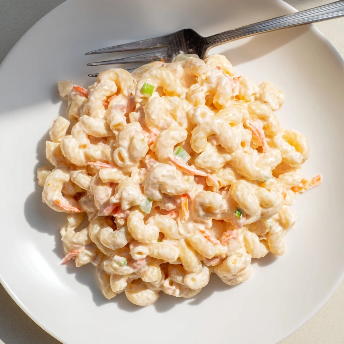 Creamy Hawaiian macaroni salad piled high with grated carrots and celery in a white serving bowl