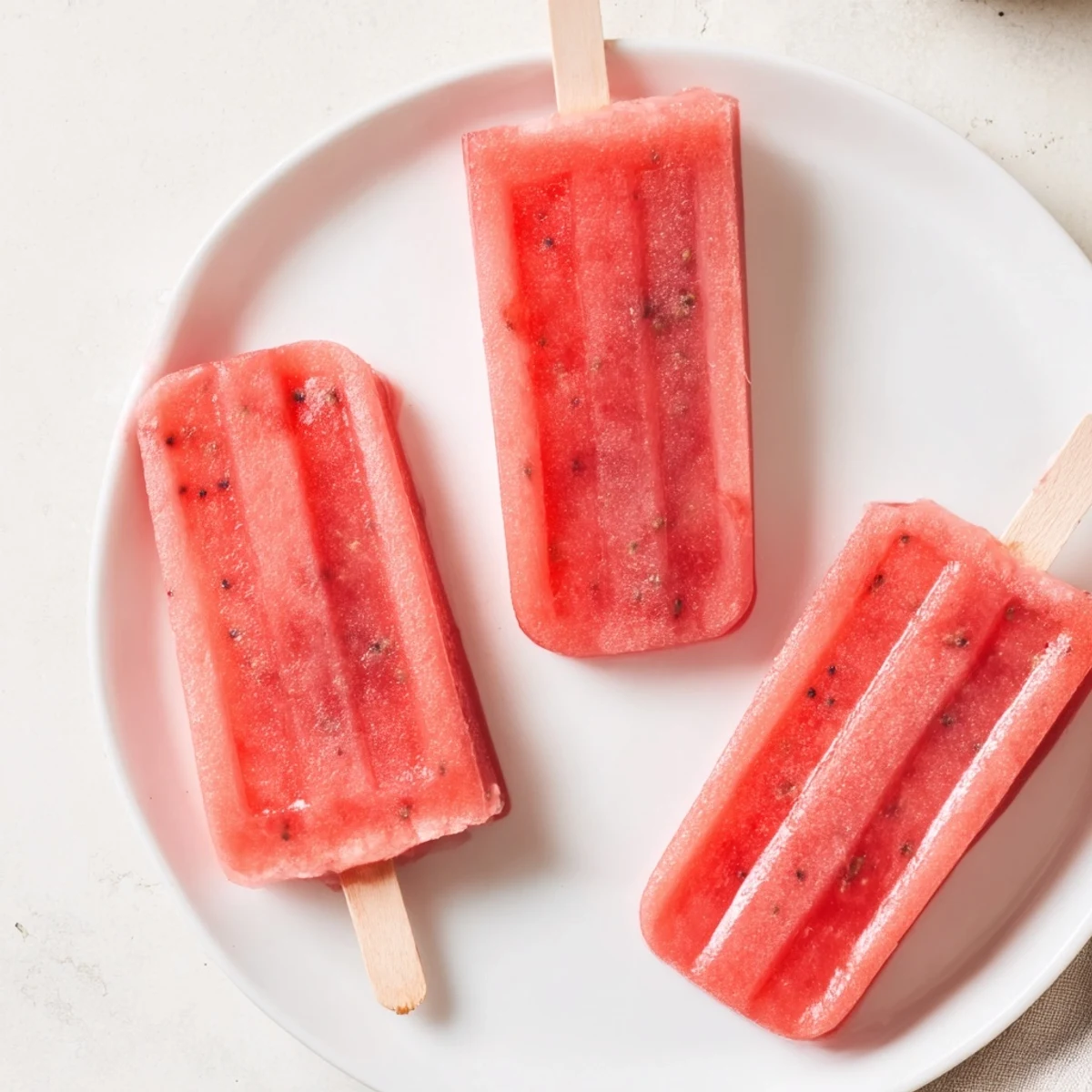 Fresh strawberry watermelon popsicles stacked on wooden board with visible fruit chunks and seeds
