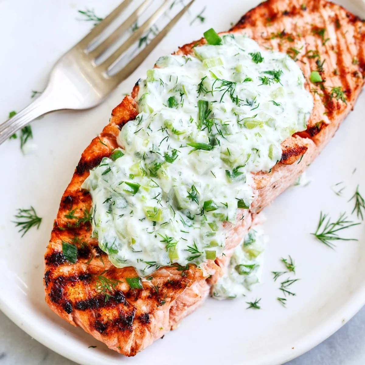 Golden grilled salmon fillets with charred grill marks drizzled with creamy cucumber dill sauce