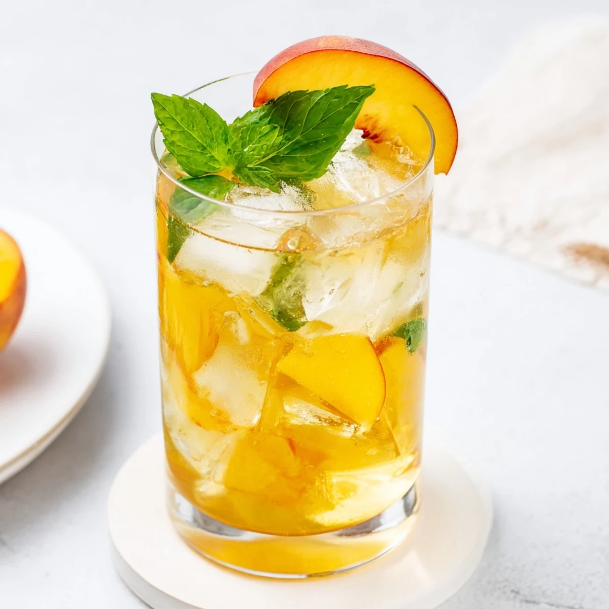 Pitcher of bright orange fresh peach lemonade drink poured over ice with fresh peach wedges on the rim