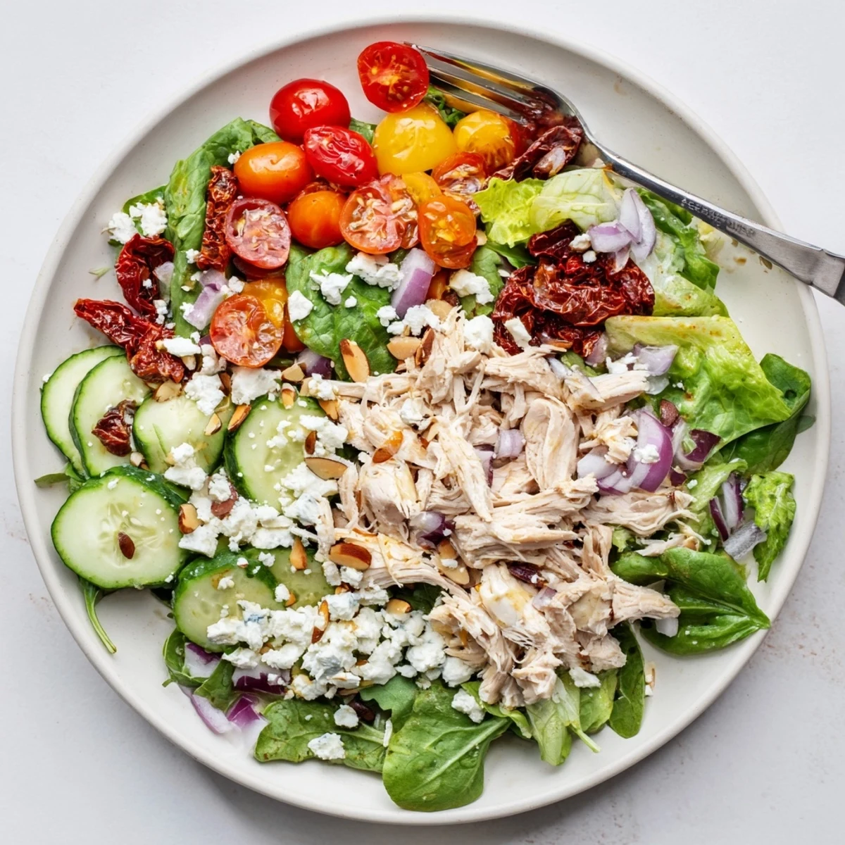Protein-packed sun-dried tomato chicken salad bowl topped with cherry tomatoes, cucumber, and toasted pine nuts
