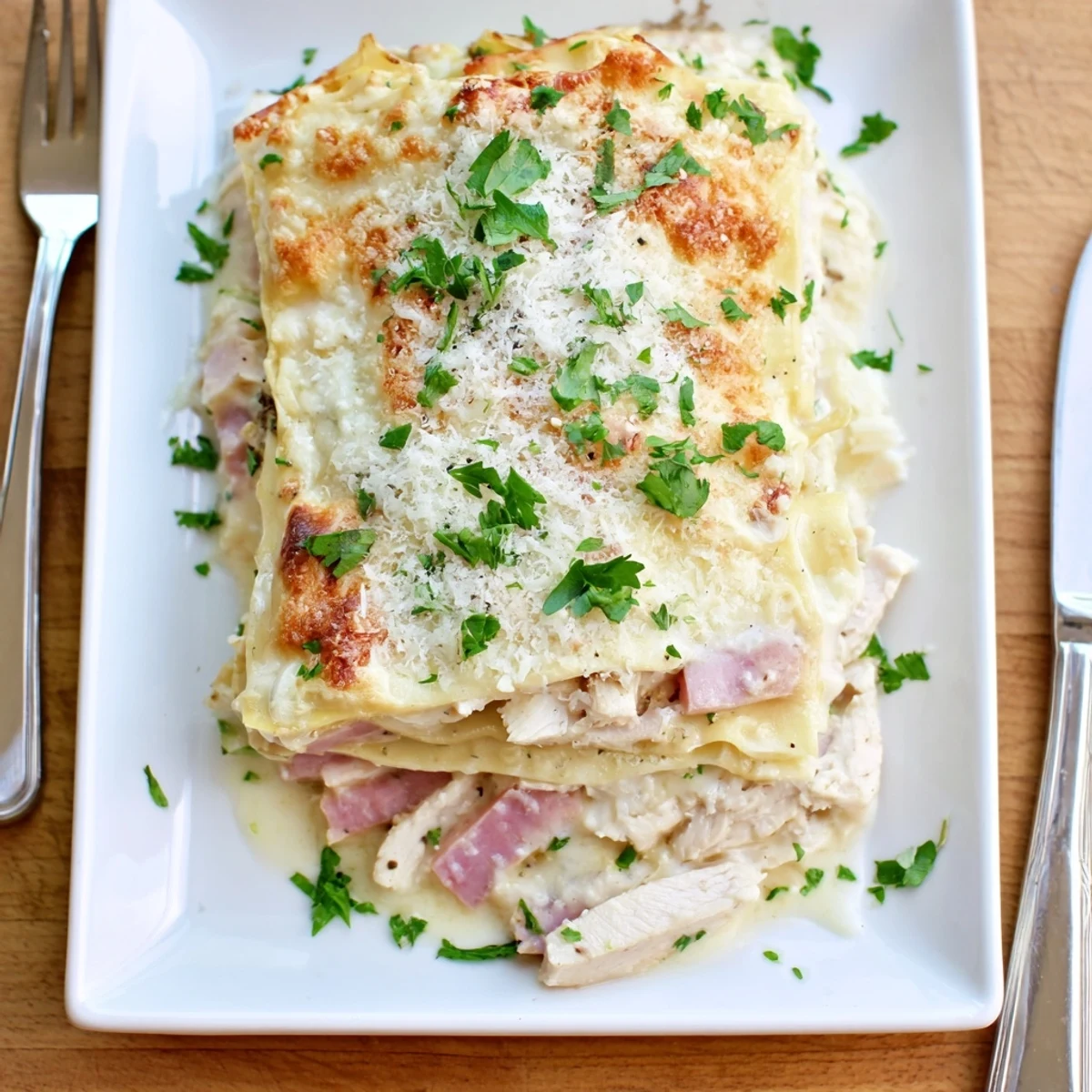 Golden bubbly chicken cordon bleu lasagna with melted Swiss cheese and fresh parsley garnish