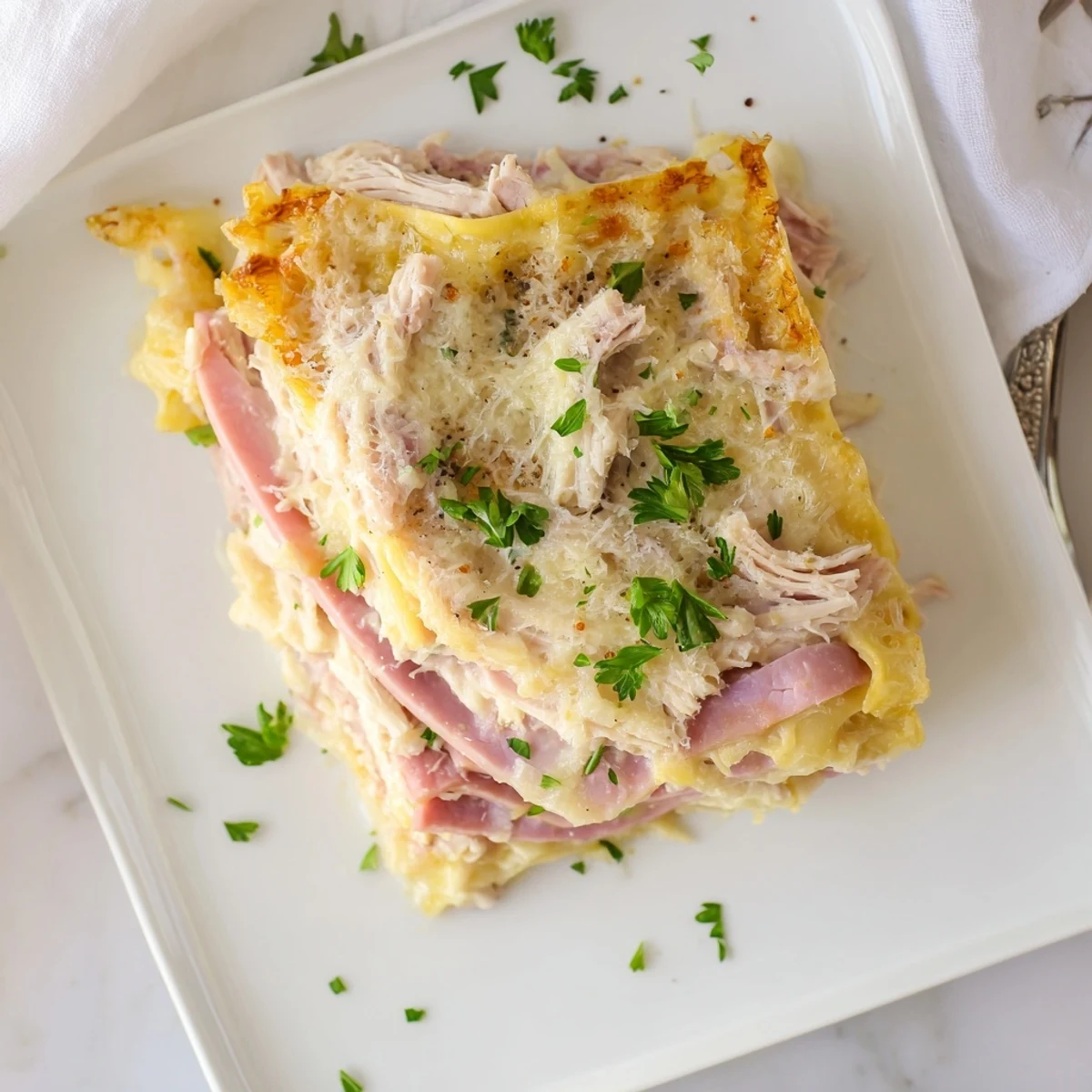 Baked chicken cordon bleu lasagna layers showcasing ham, creamy sauce, and browned cheese topping