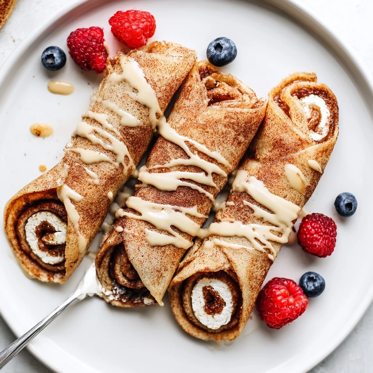 Stack of Cinnamon Roll Protein Crepes topped with protein glaze and berries