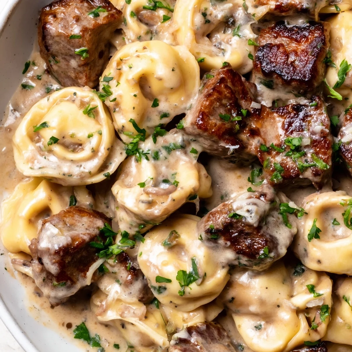 Golden seared steak bites nestled over cheese tortellini in garlic cream sauce