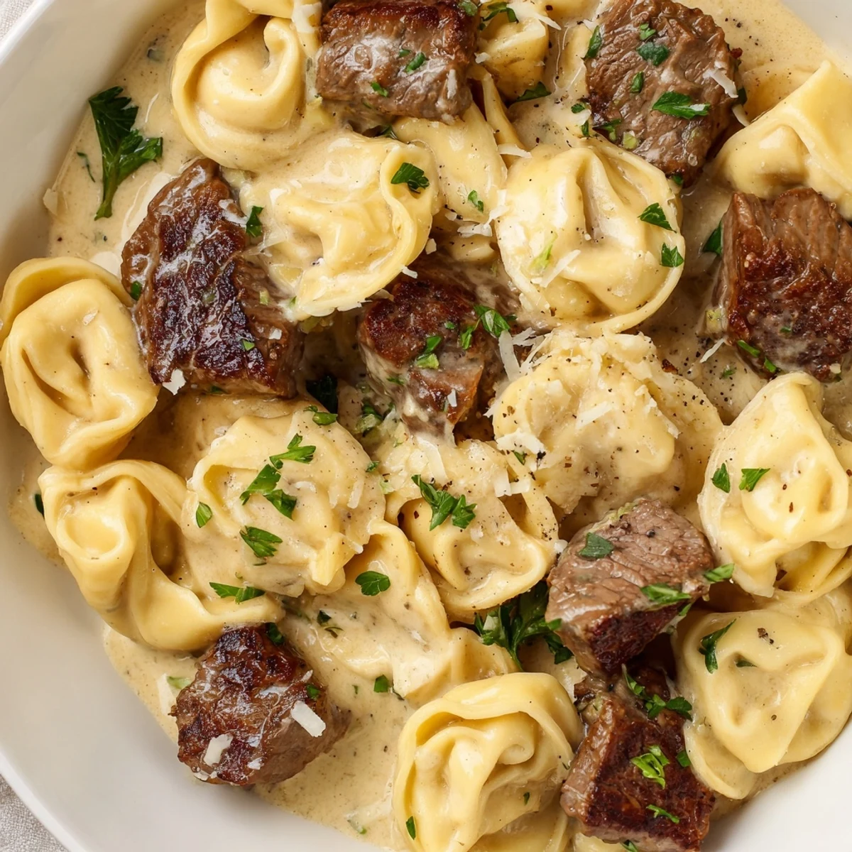 Steaming bowl of garlic steak tortellini coated in rich Parmesan cream sauce