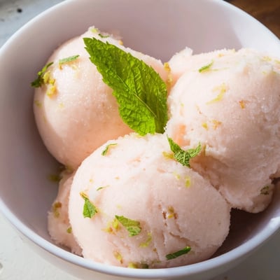 Vibrant pink sorbet with mint garnish, served in a waffle cone beside sliced lemons and mint sprigs.  